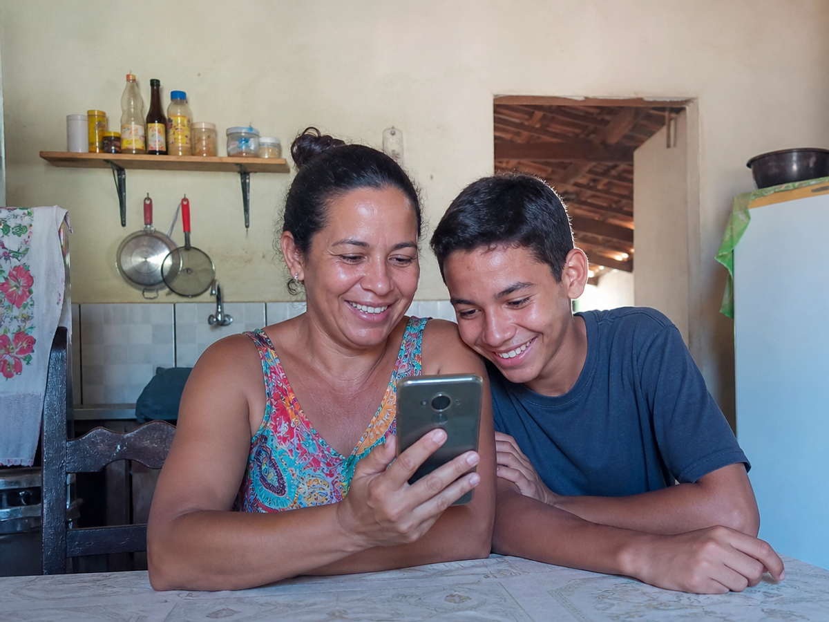 Mãe e filho adolescente olhando juntos o celular na cozinha de casa